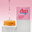 A conditioner bar floating on water with a pink box of the product labeled 'Dip' in the background, against a pink backdrop.